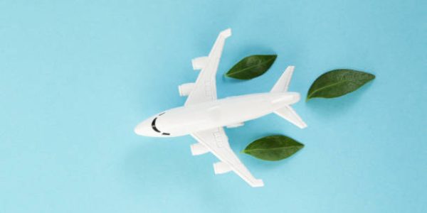 White airplane model emitting fresh green leaves on blue background. Sustainable travel; clean and green energy; and biofuel for aviation industry concept.