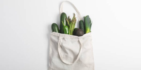 Reusable zero waste textile product bag filled with green vegetables, top view on white background