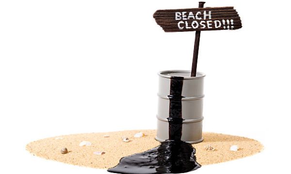 Leaking oil drum with "Beach Closed" sign sitting on sand with sea shells.